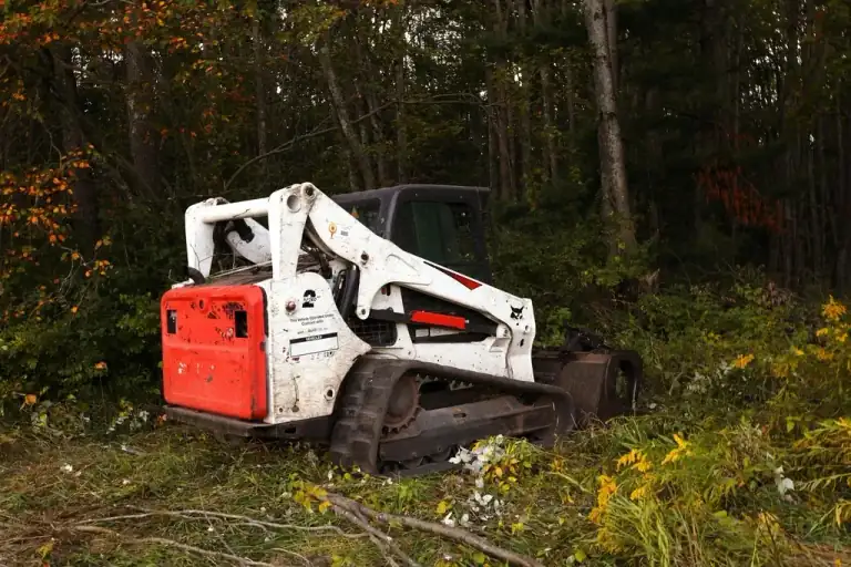 Compact track loader clearing an overgrown wooded lot down to open, usable ground in the Cincinnati tri-state area