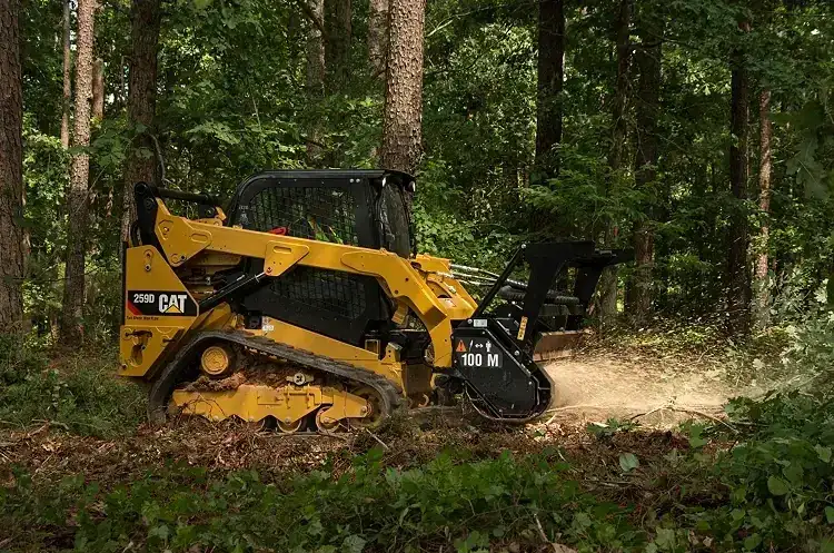 CAT compact track loader with a forestry mulching head grinding brush and undergrowth in a wooded lot